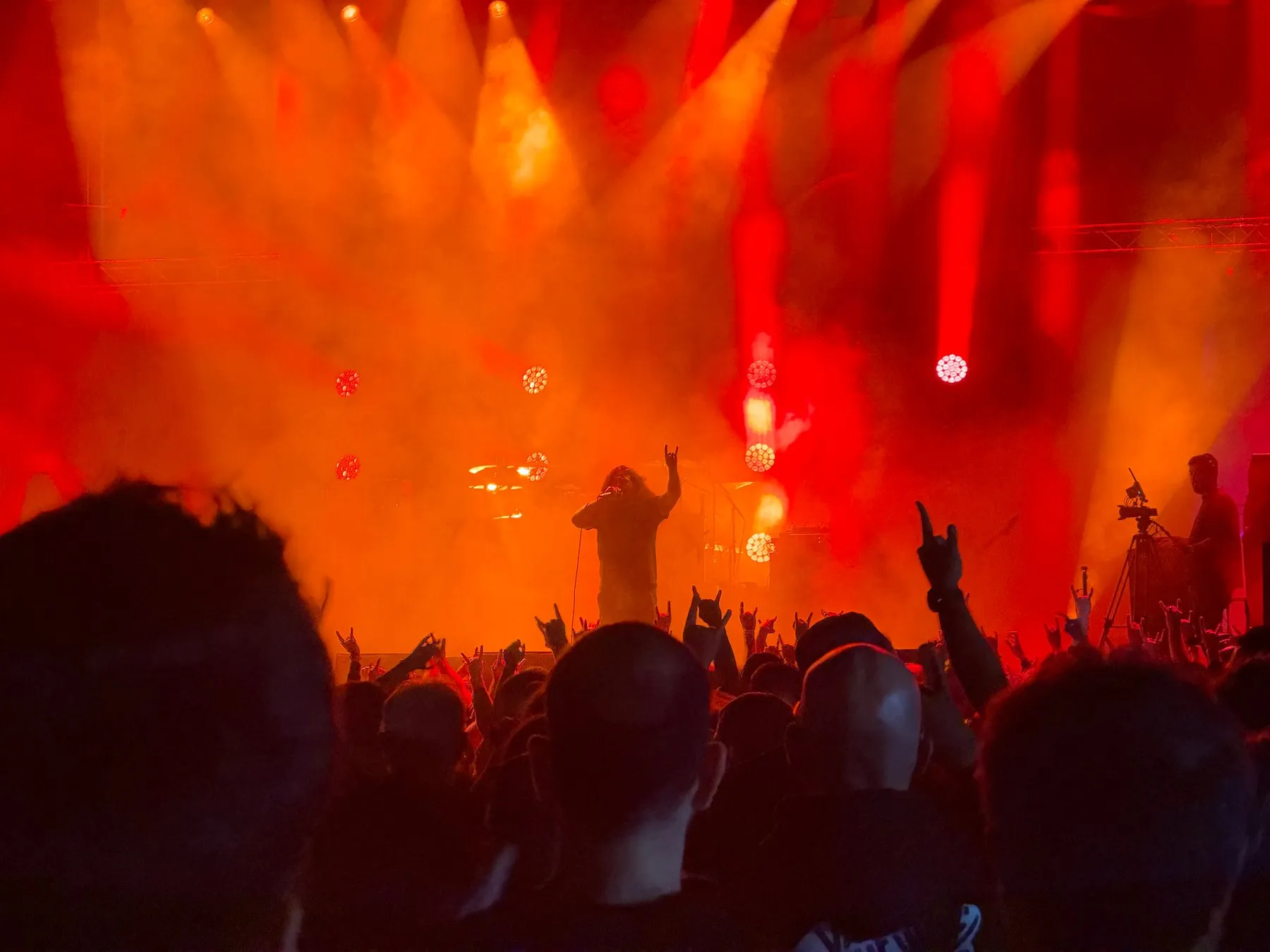 Kataklysm's singer facing a crowd of raised hands beneath orange lights